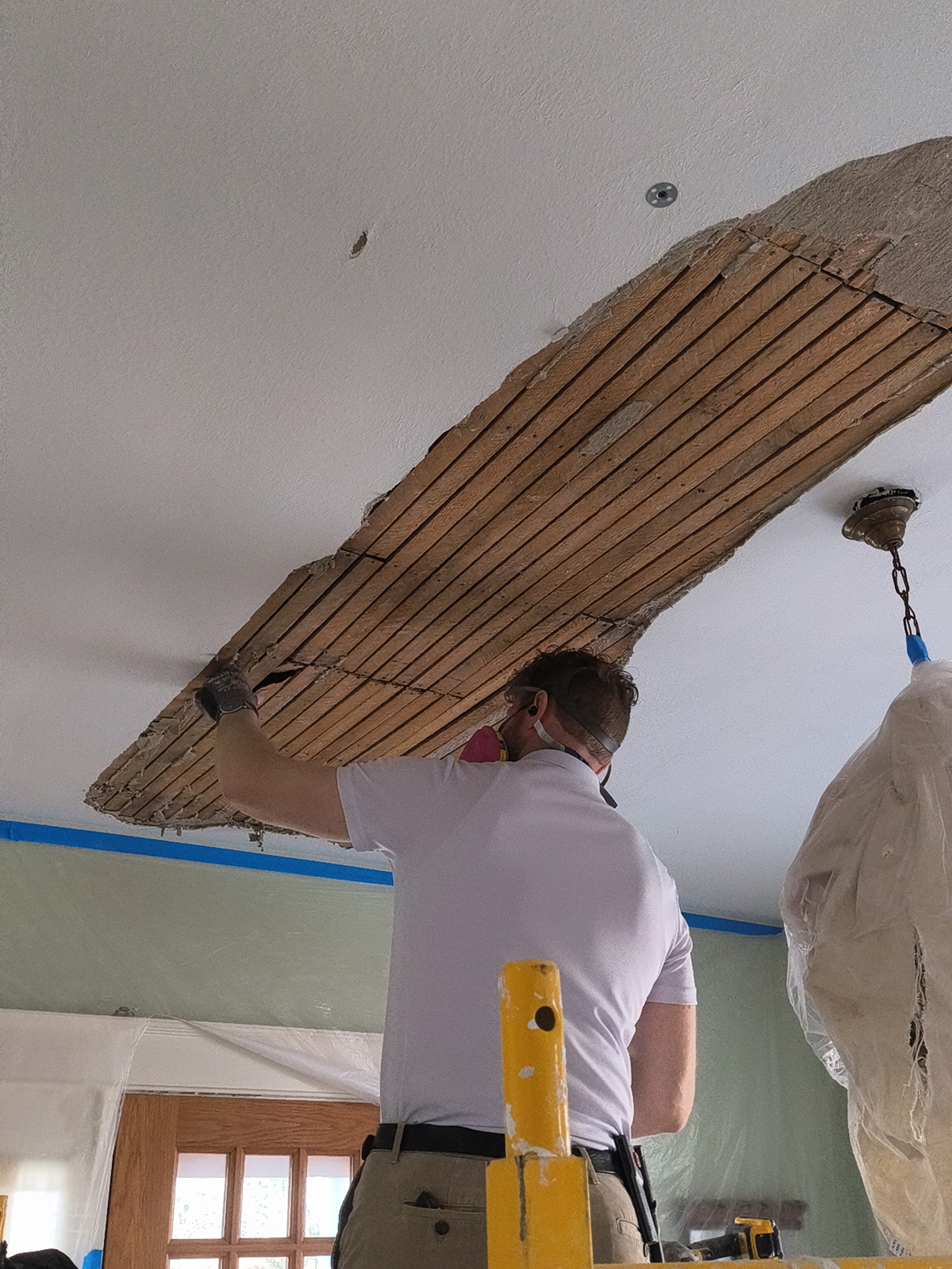 MN Plastering LLC technician removing damaged ceiling plaster section to expose original wood lath during repair